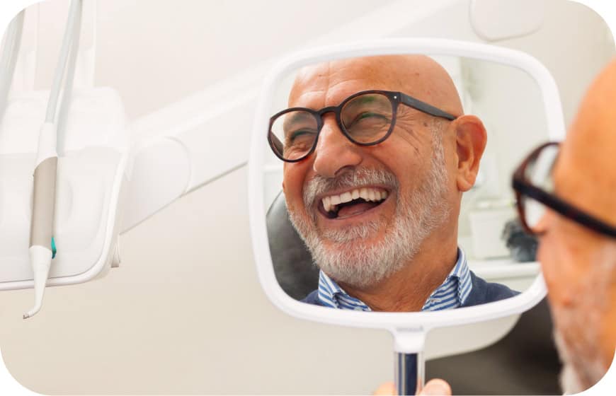 Smiling elderly man looking at his reflection in dental mirror during check-up.
