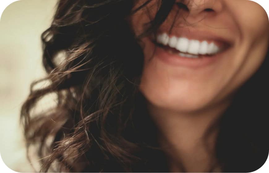 Close-up of a woman's smiling mouth showing white teeth and curly hair.
