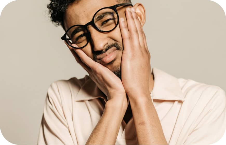 Man with glasses touching his face, smiling gently, in a beige shirt.